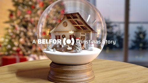 Snow globe on a wooden table, with a decorated Christmas tree visible in the background. The image features the words ‘A BELFOR Christmas story’.