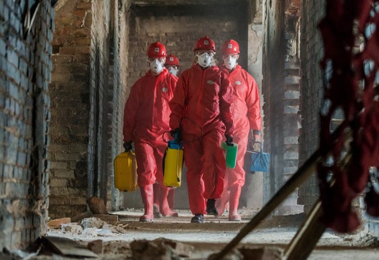 Employees in red PPE suits walking in a damaged structure